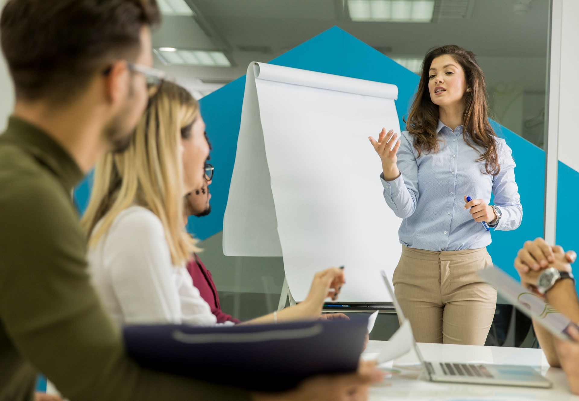 Confident young team leader giving a presentation to a group of young colleagues as they sit grouped by the flip chart in the small startup office